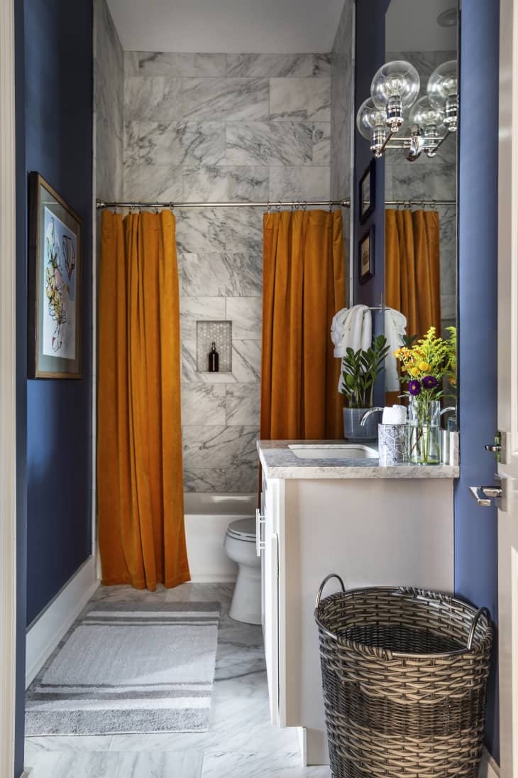 Two orange shower curtains are installed in a bathroom with blue walls and marbled tile.