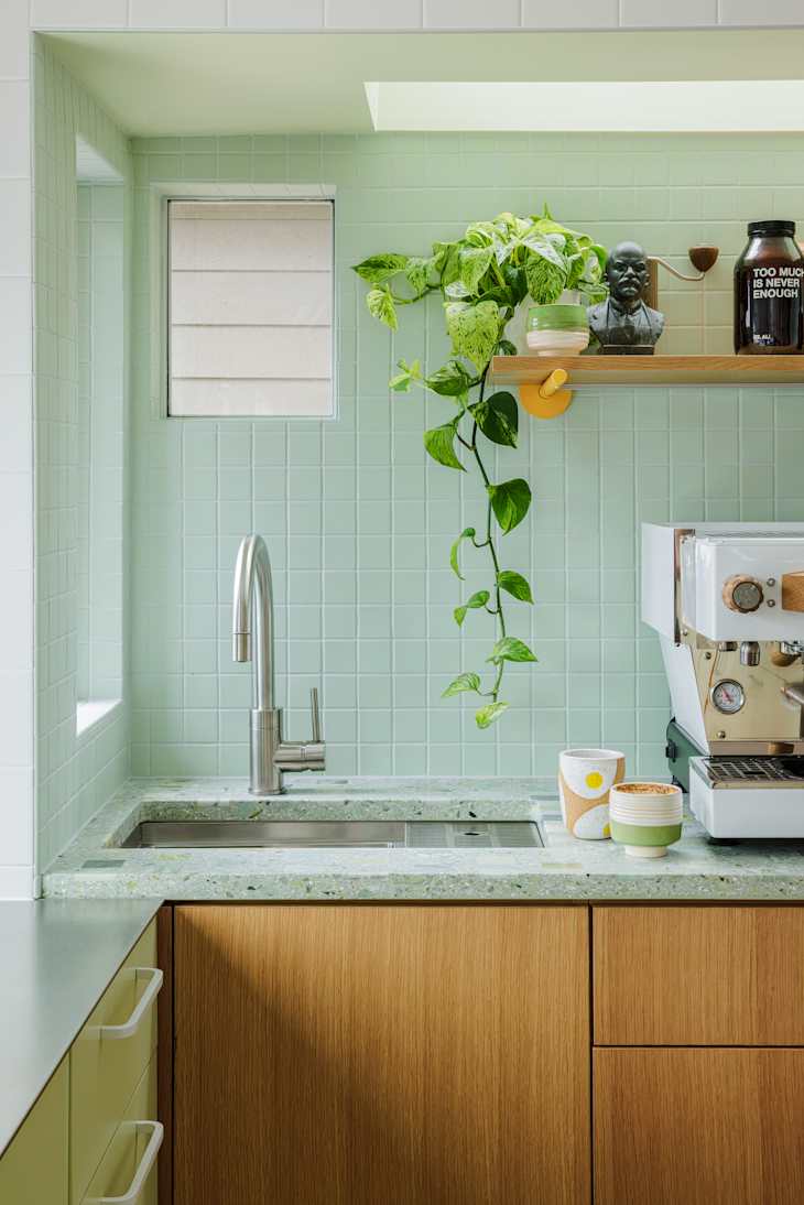 Modern kitchen with mint green tiled walls, a stainless steel faucet, and a coffee machine on a speckled countertop.