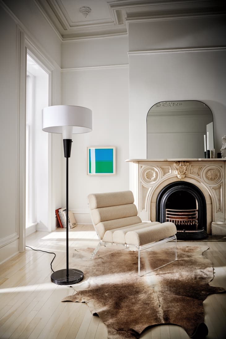 Elegant living room with a beige lounge chair, floor lamp, ornate fireplace, and abstract art on the wall.