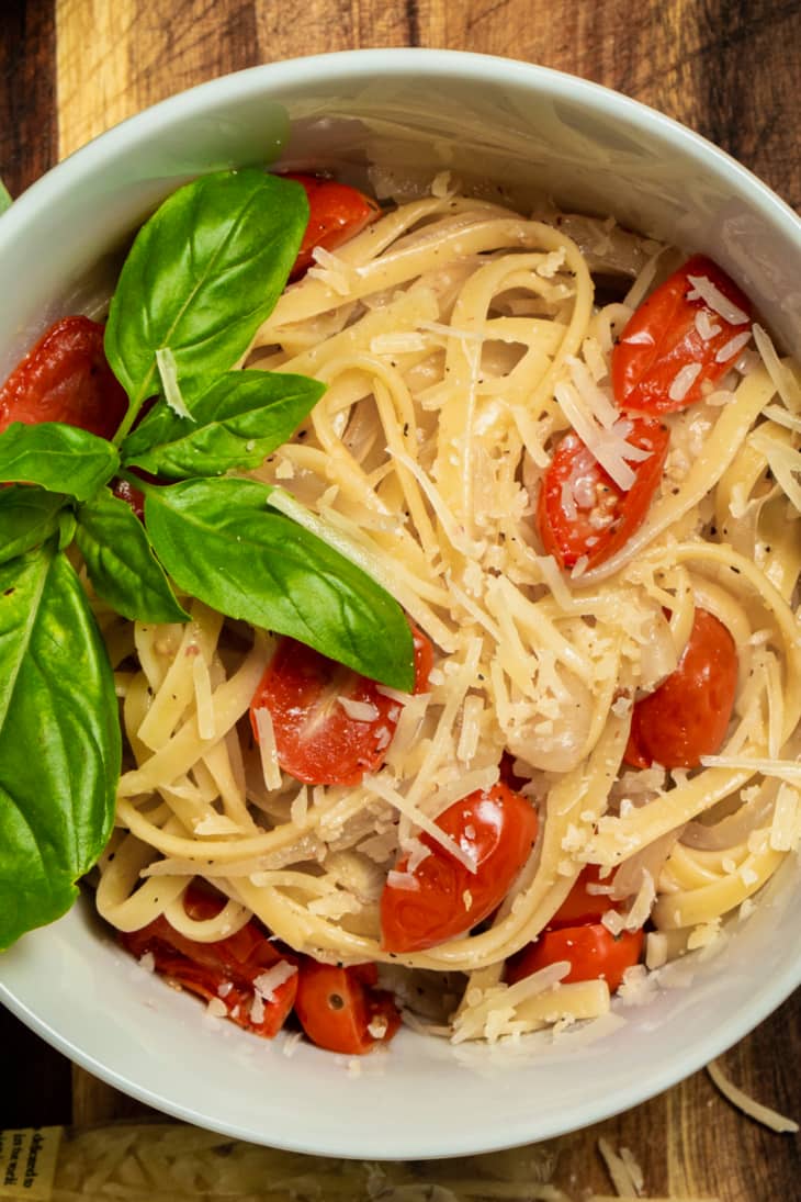 bowl of spaghetti with cherry tomatoes and basil leaves on a wooden table
