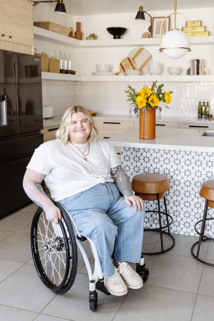 Person in a wheelchair in a modern kitchen with open shelves, sunflowers on the counter, and bar stools.