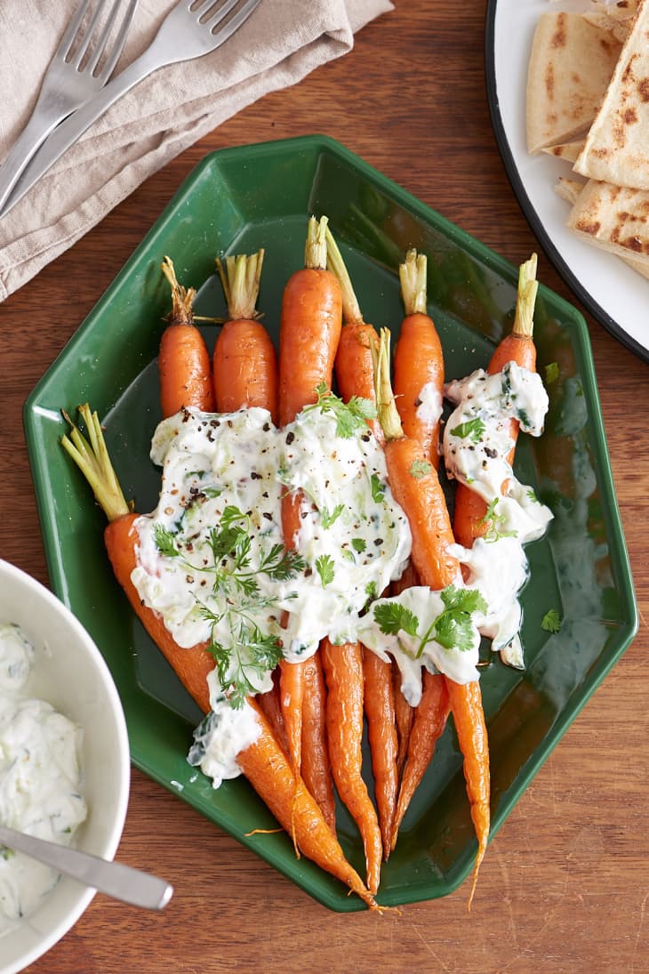 Roasted carrots topped with creamy raita and cilantro on a green plate, served with flatbread.