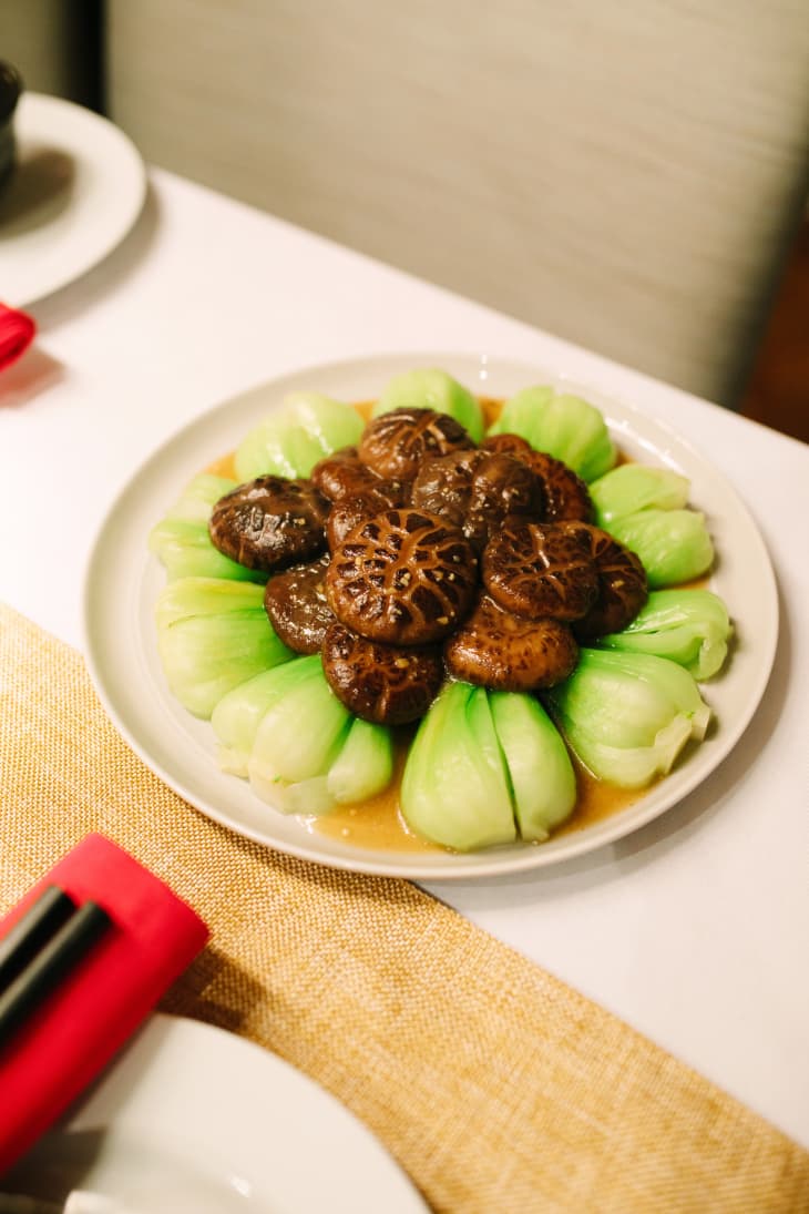 Steamed bok choy and shiitake mushrooms arranged on a white plate with sauce.