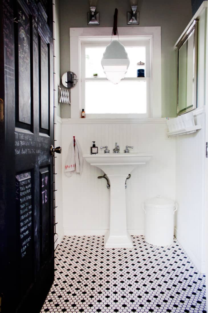 Bathroom with pedestal sink, hexagonal black and white tile floor, wall mirror, and hanging light fixture.