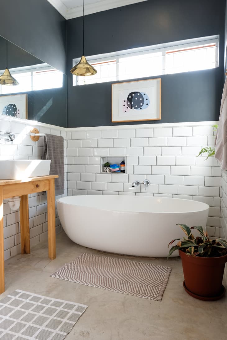 Modern bathroom with a white freestanding tub, wooden vanity, potted plant, and geometric wall art.