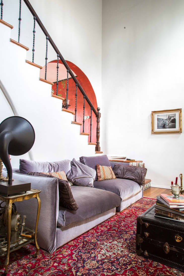 Gray sofa with patterned cushions on a red Persian rug, vintage gramophone, and staircase with red archway.