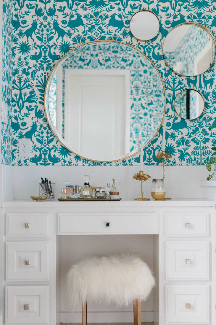 One large round mirror surrounded by three smaller round mirrors on a wall with teal patterned wallpaper
