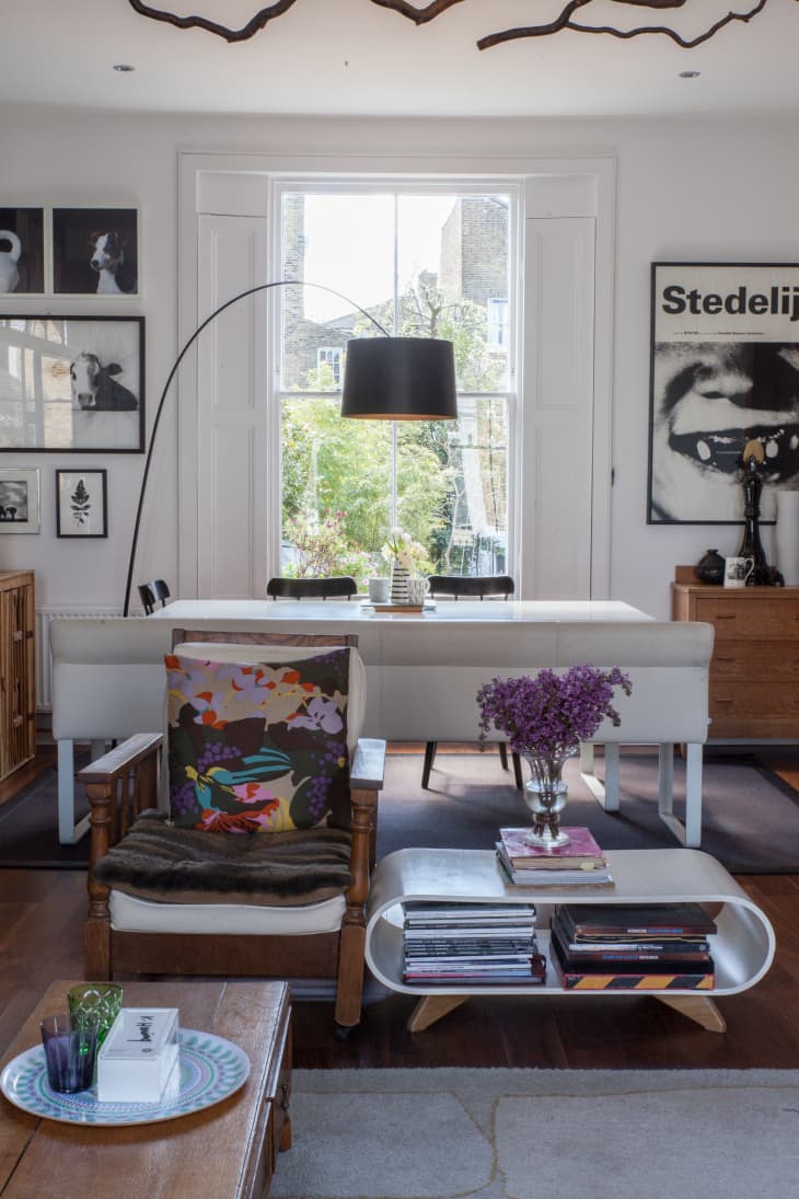 Living room with a wooden armchair, colorful cushion, modern coffee table, purple flowers, and large window with garden view.