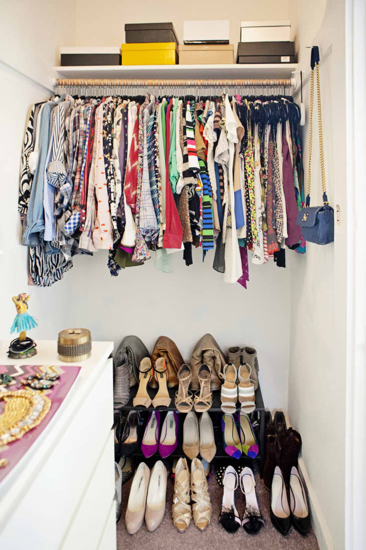 Organized closet with colorful clothes on hangers, shoes neatly arranged below, and boxes on the shelf above.