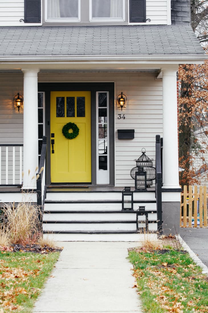 Front porch with yellow door, wreath, black lanterns, and birdcage decor.