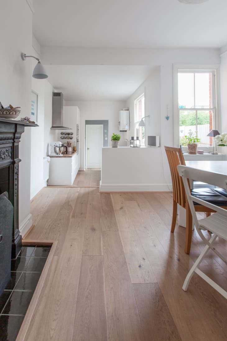 Open-plan kitchen and dining area with wooden floors, white walls, a round table, and potted plants by the window.