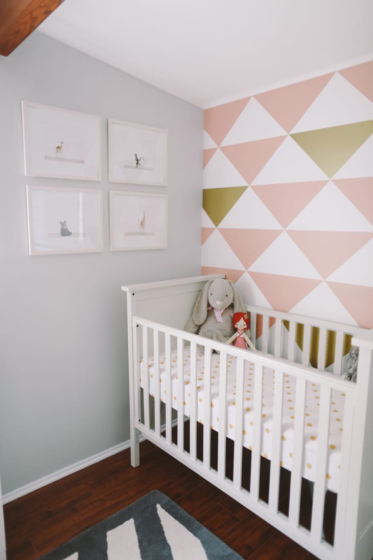 White crib with polka dot bedding, stuffed bunny, and doll in a nursery with geometric accent wall and framed animal prints.