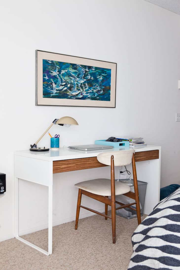 Home office with a white desk, wooden chair, desk lamp, and abstract blue artwork on the wall.