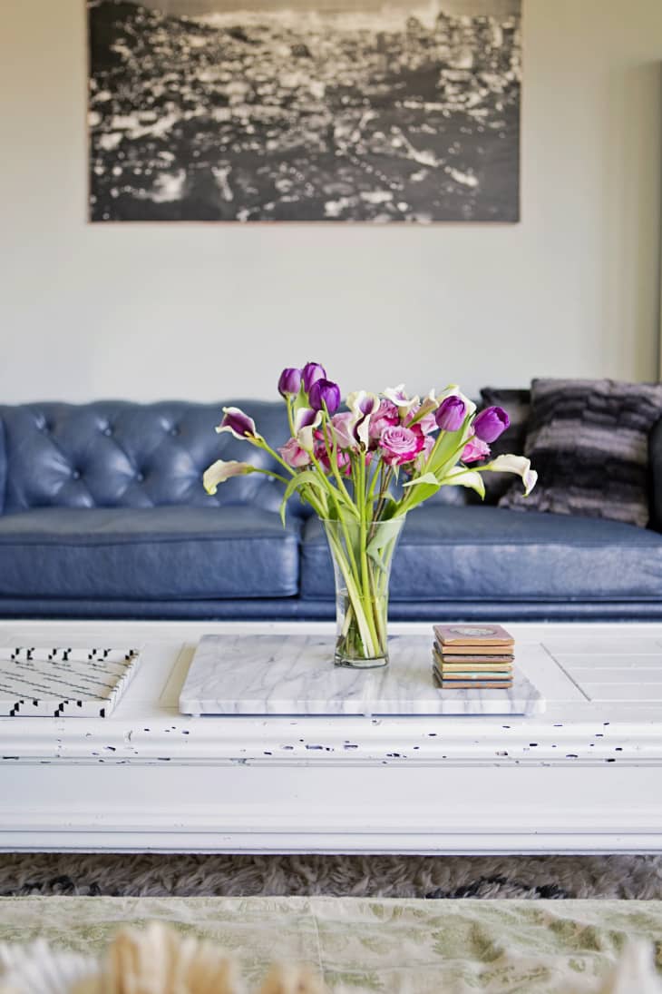 Vase of purple and white flowers on a white coffee table, blue sofa, and black-and-white cityscape photo on the wall.