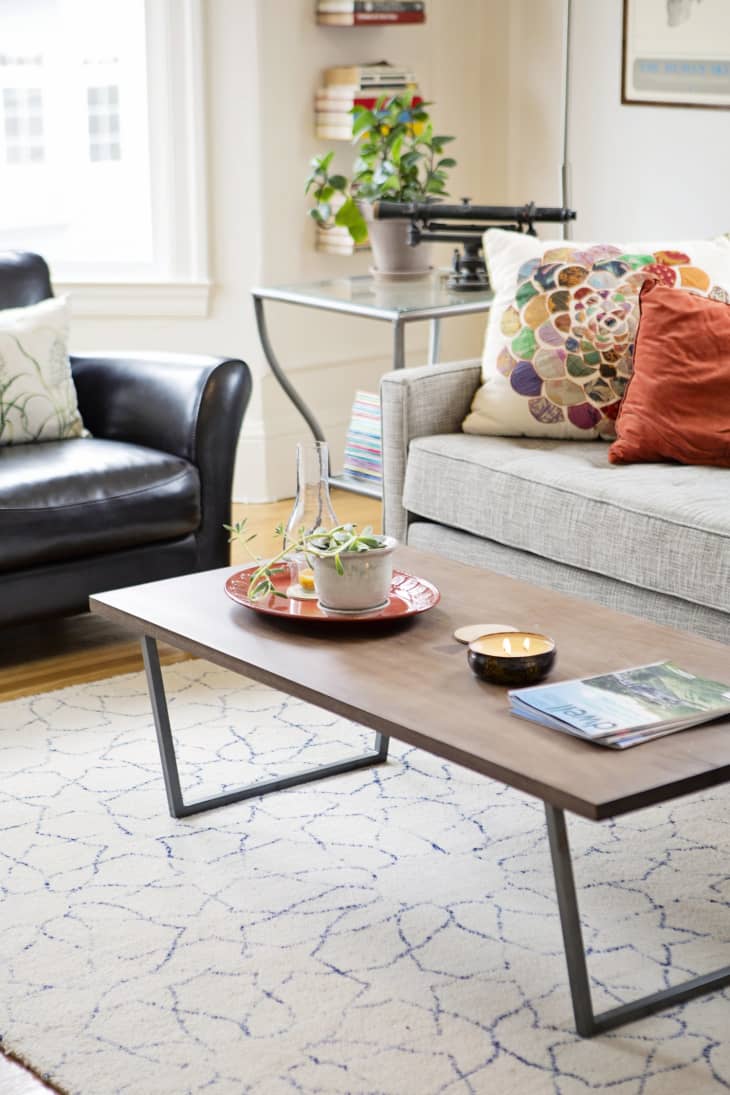 Living room with gray sofa, colorful pillows, black leather chair, wooden coffee table, and potted plant on side table.