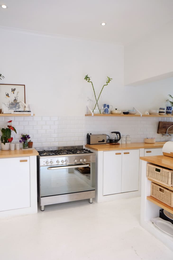 Modern kitchen with white cabinets, wooden countertops, stainless steel oven, and open shelves with plants and decor.