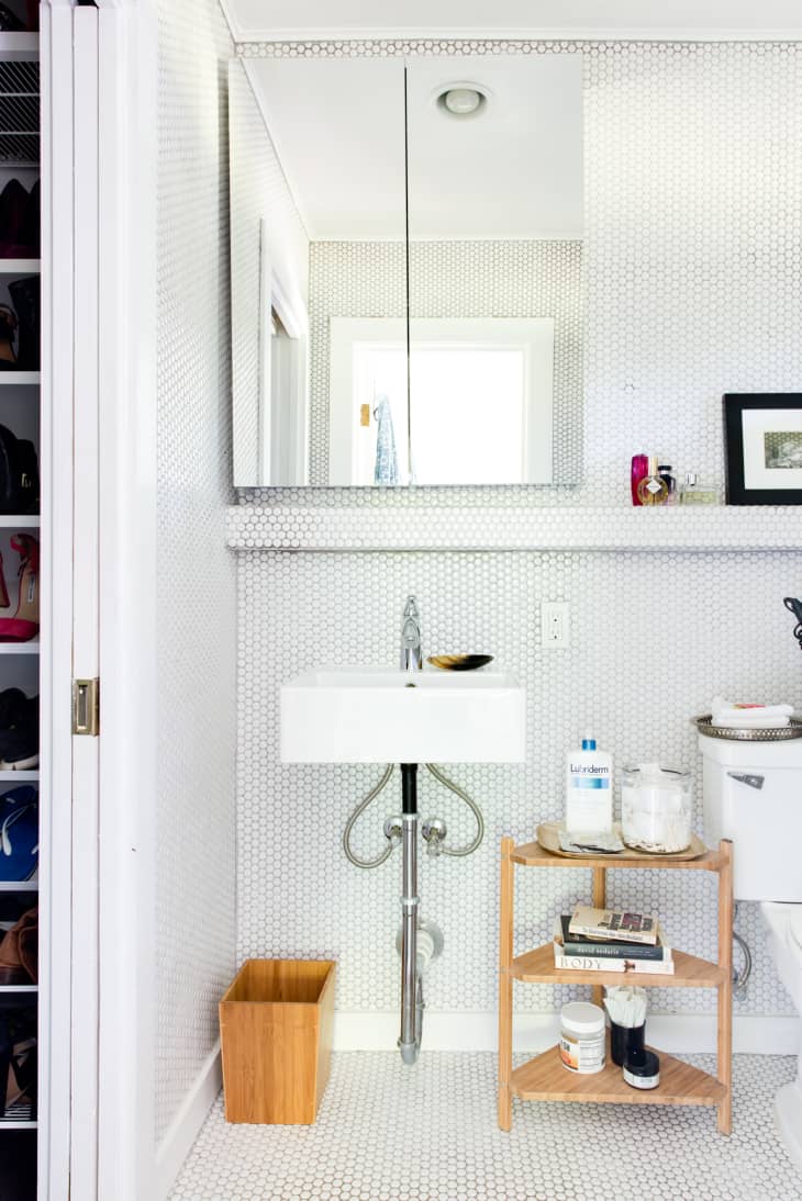 A small wooden shelf is placed underneath a pedestal sink for extra storage.