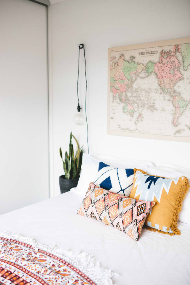 Bed with patterned pillows, a hanging bulb, a potted plant, and a vintage world map on the wall.