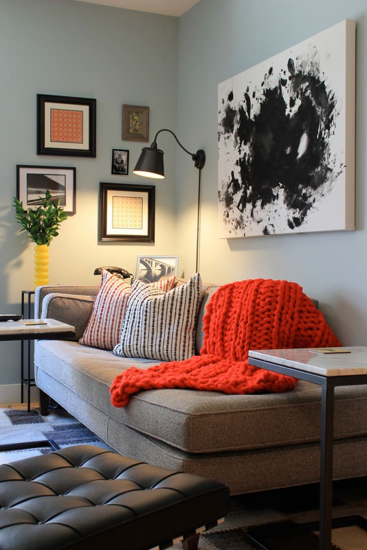 Cozy living room with a gray sofa, red knit throw, striped pillows, abstract wall art, and framed photos.