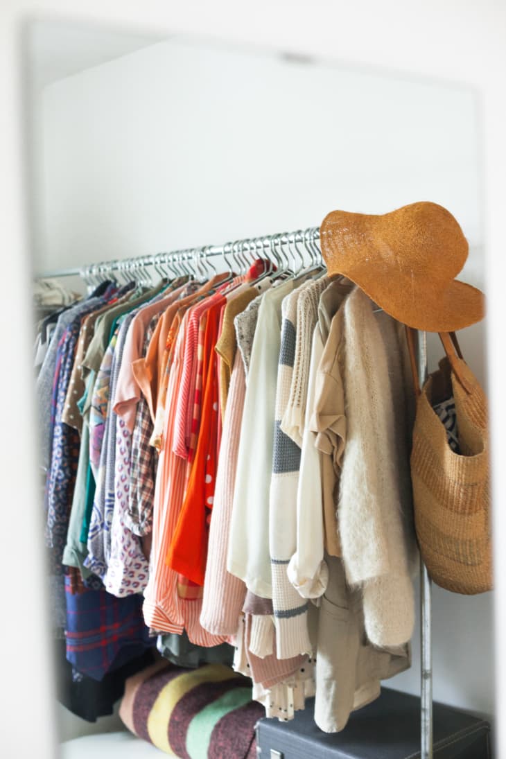Clothing rack with colorful shirts, sweaters, a straw hat, and a woven bag.