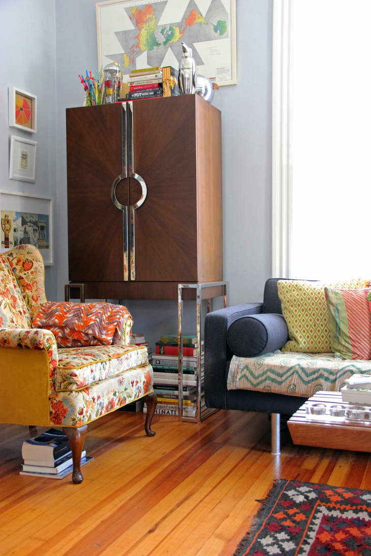 Floral armchair and blue sofa in a cozy living room with books, colorful pillows, and a wooden cabinet.