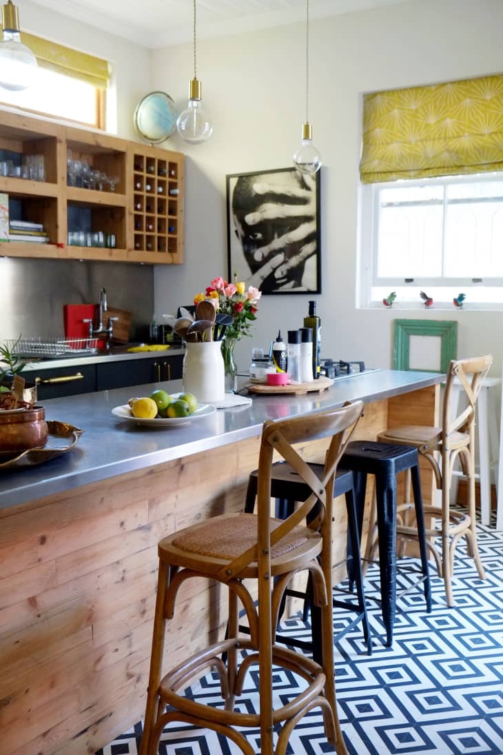 Wooden kitchen island with bar stools, geometric floor tiles, hanging lights, and a vase of flowers.