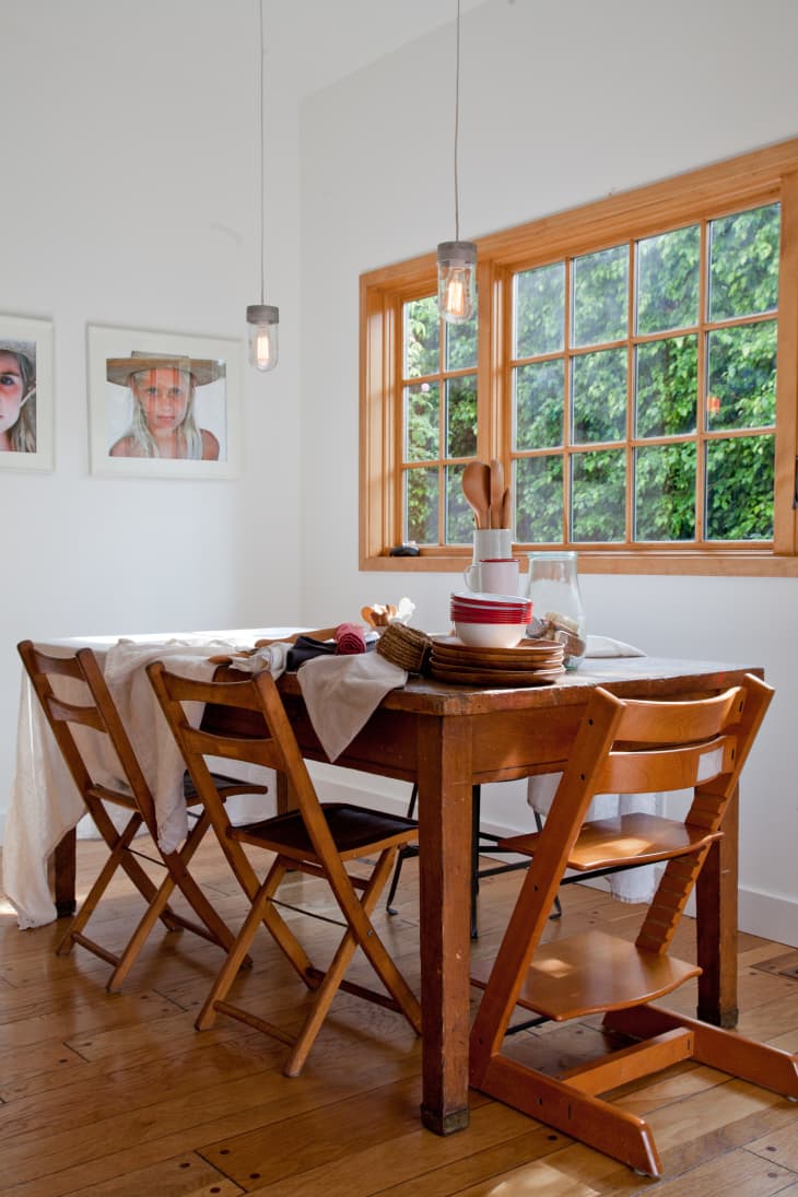 Dining room with wooden table, folding chairs, tableware, and large window with garden view.