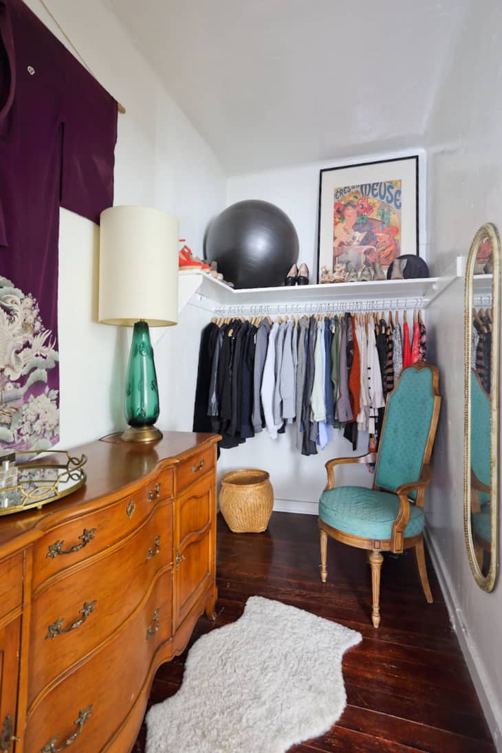 Vintage-style closet with wooden dresser, green chair, clothes rack, framed poster, and exercise ball.