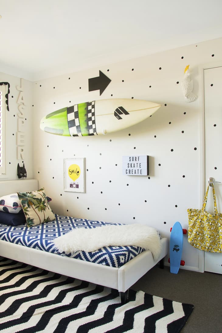 Kids' room with surfboard wall decor, polka dot wall, blue skateboard, zigzag rug, and bed with geometric bedding.