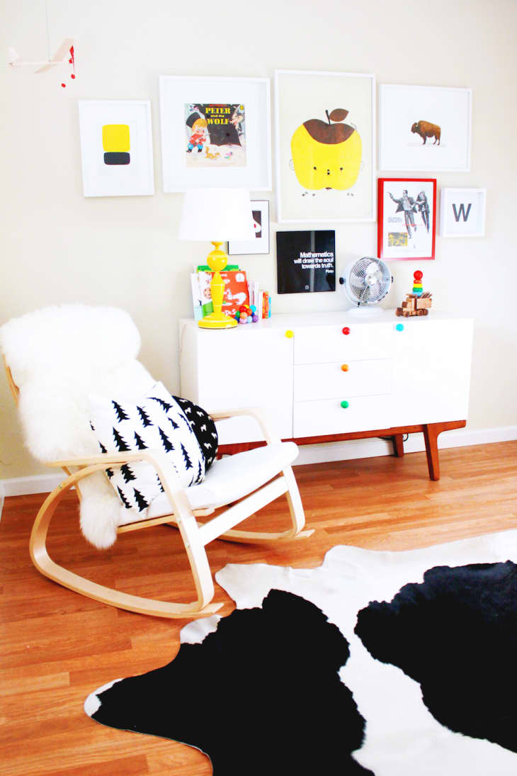 Nursery with a white dresser, colorful knobs, rocking chair, tree pillow, and framed art on the wall.
