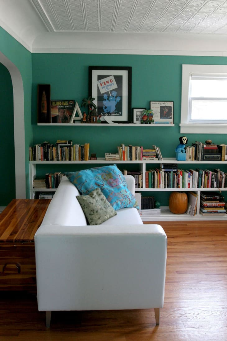 White sofa with colorful pillows in a living room, green walls, bookshelves, and framed art.