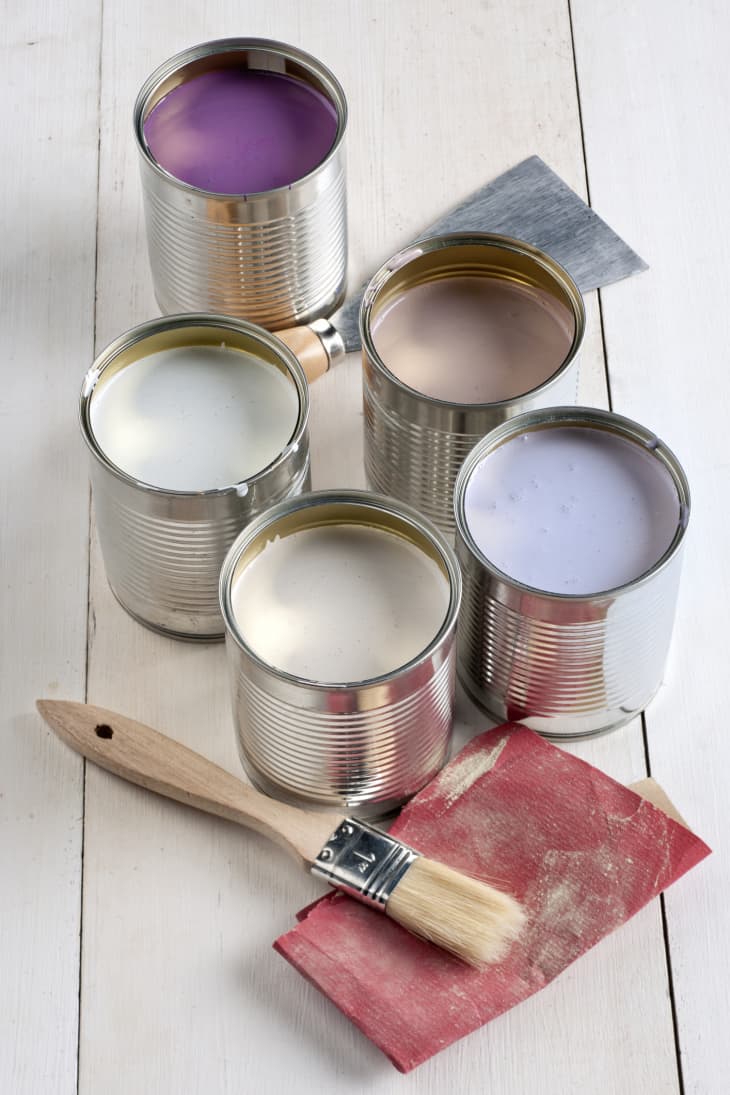 5 canisters of paint colors with 2 types of paint brushes on wood floor
