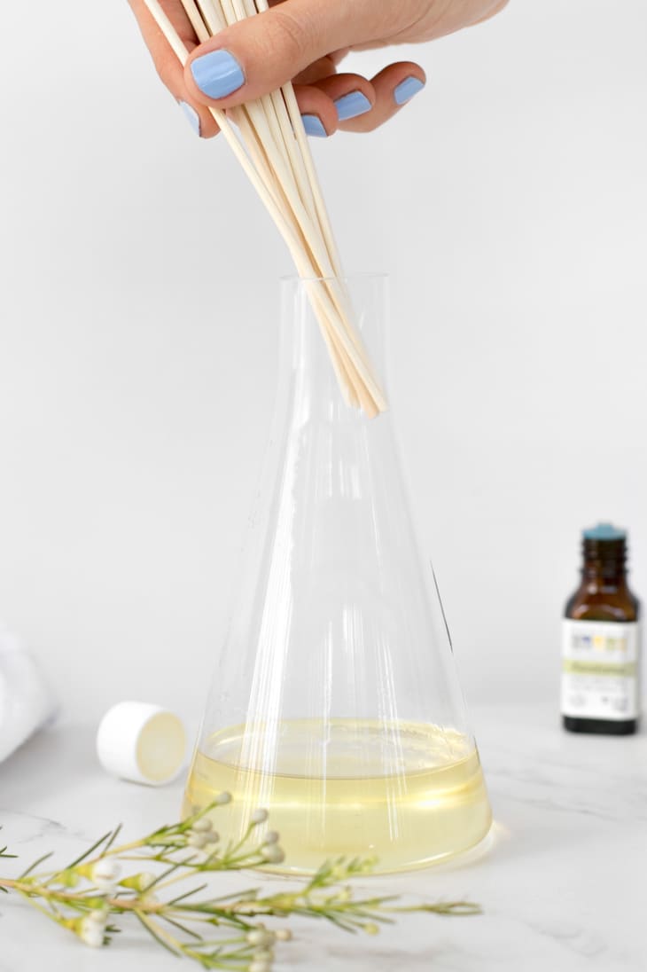 Person dipping reeds into oil-based solution inside glass container