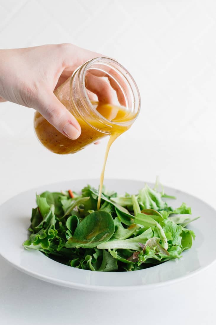 Pouring vinaigrette from a jar over a plate of salad