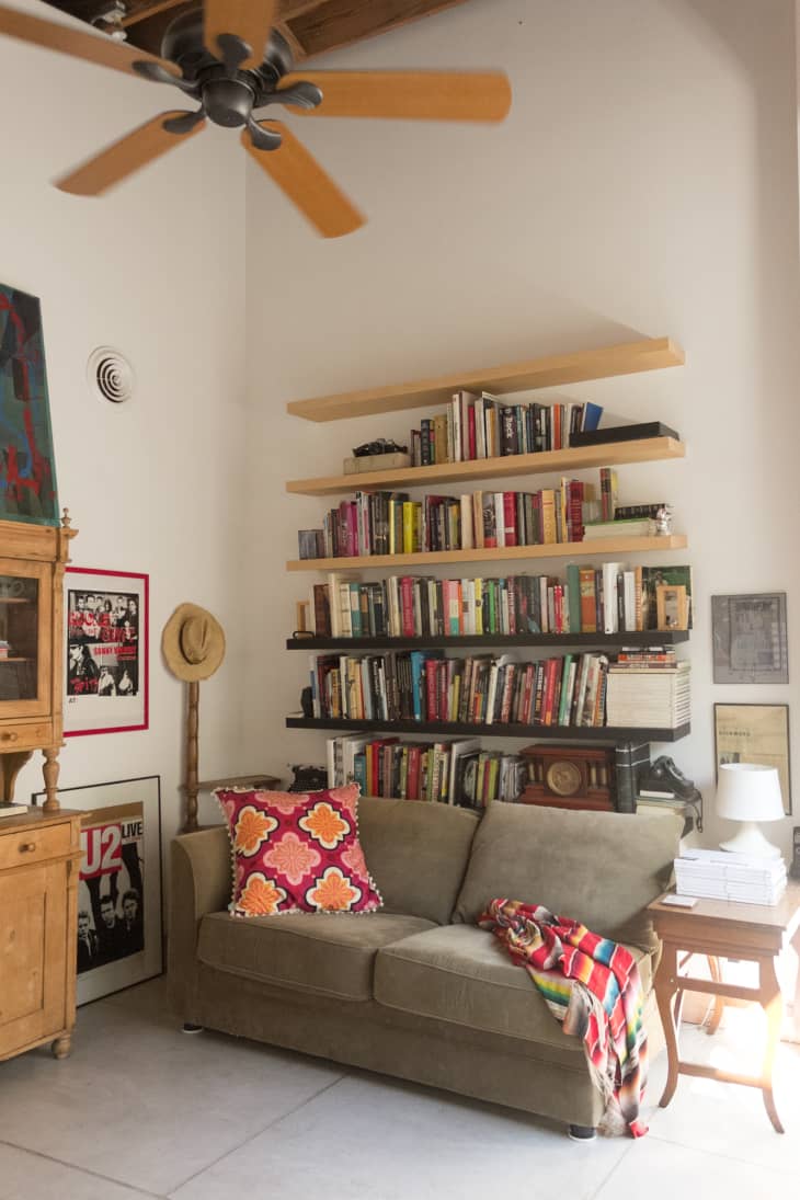 Cozy living room with a beige sofa, colorful pillows, bookshelves, and framed posters on the wall.