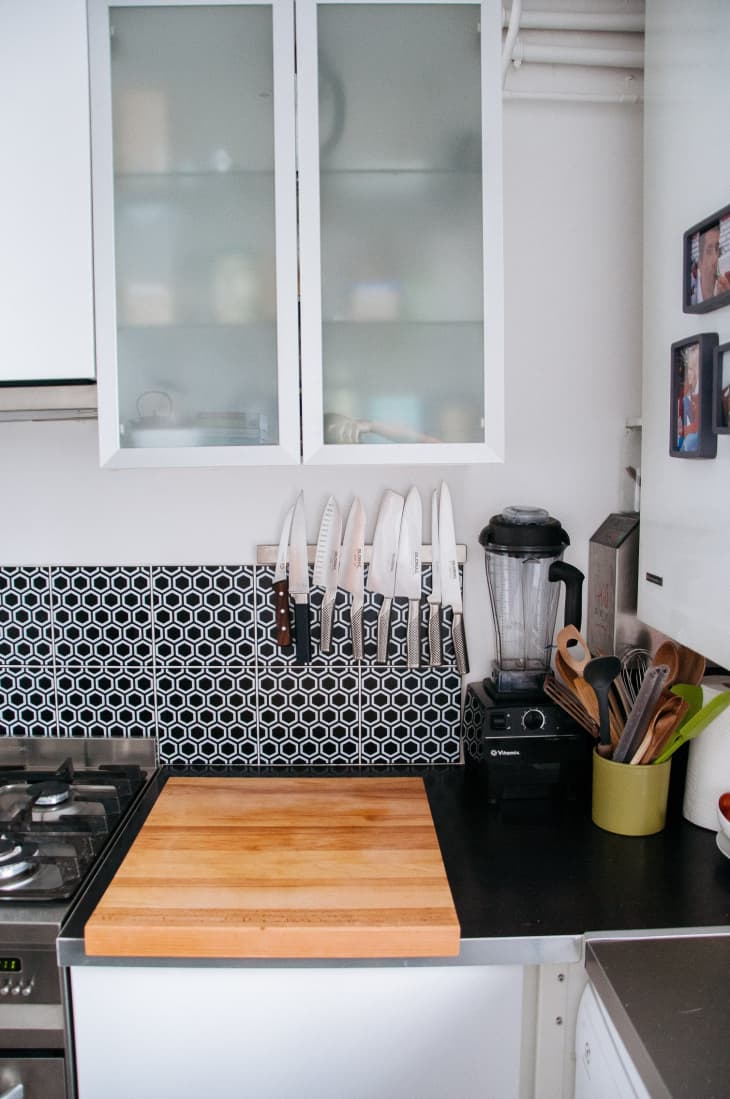 Kitchen corner with a wooden cutting board, knife rack, blender, and utensils against a geometric tile backsplash.