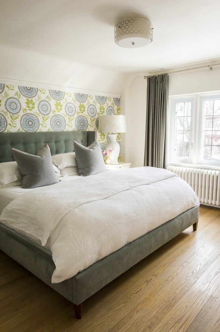 Bedroom with a large bed, green headboard, floral wallpaper, and a white lamp on a side table.