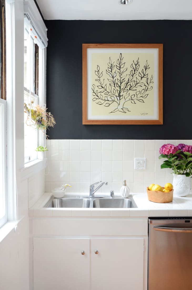 A small sink located at the corner of a kitchen decorated with a picture frame and flowers