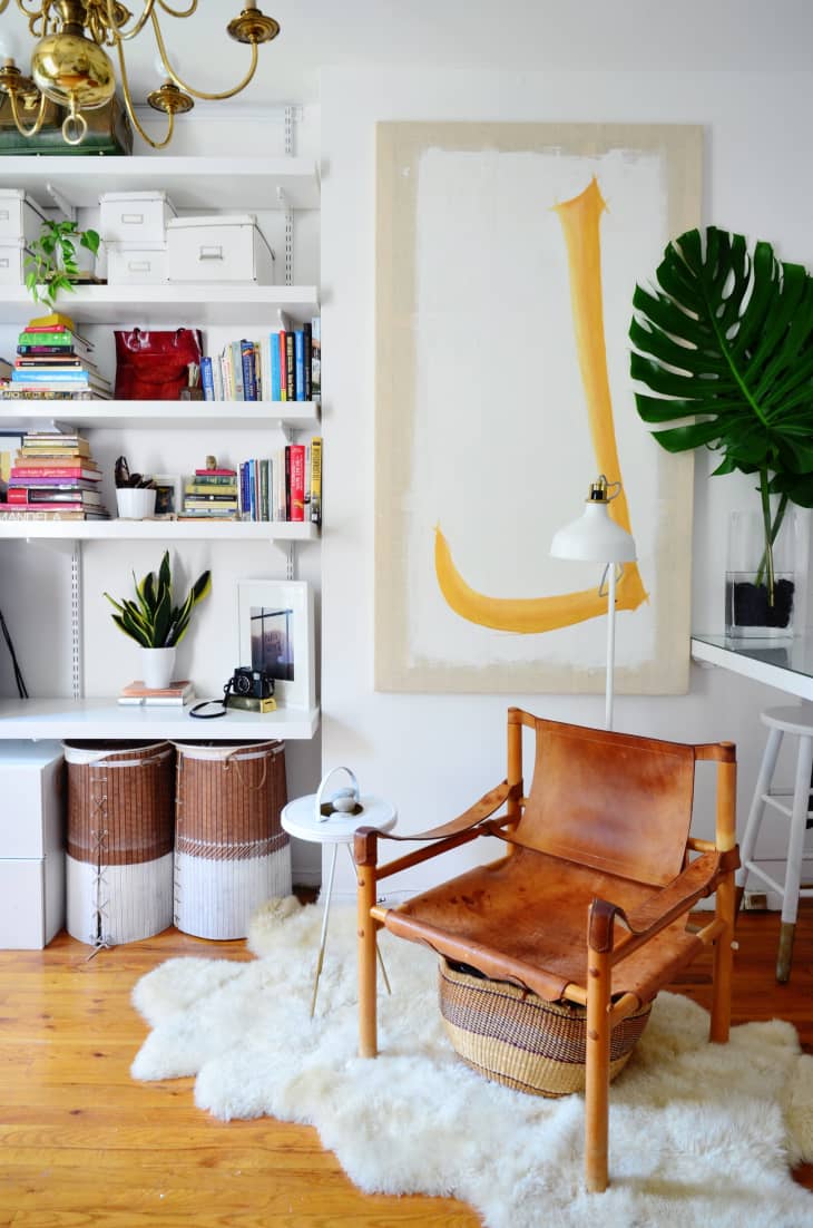 Cozy reading nook with leather chair, white rug, bookshelves, large abstract art, and a potted plant.