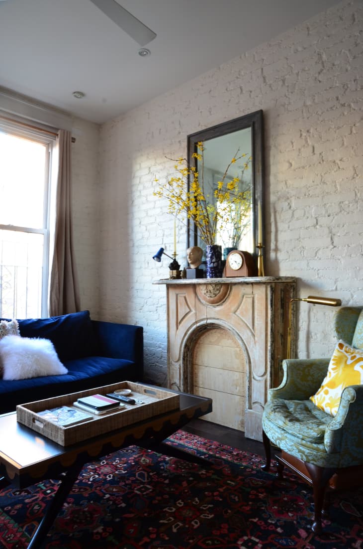 Cozy living room with blue sofa, green armchair, ornate fireplace, and yellow flowers in a vase on the mantel.