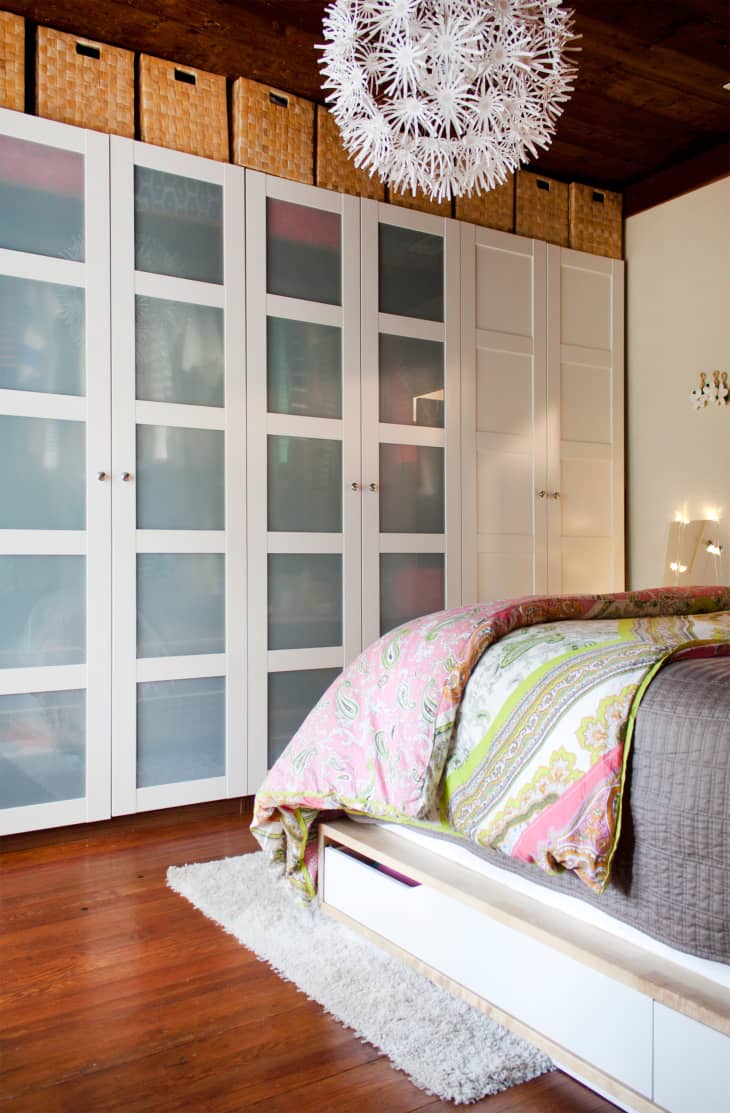 Bedroom with white wardrobes, wicker baskets, a colorful paisley bedspread, and a white pendant light fixture.