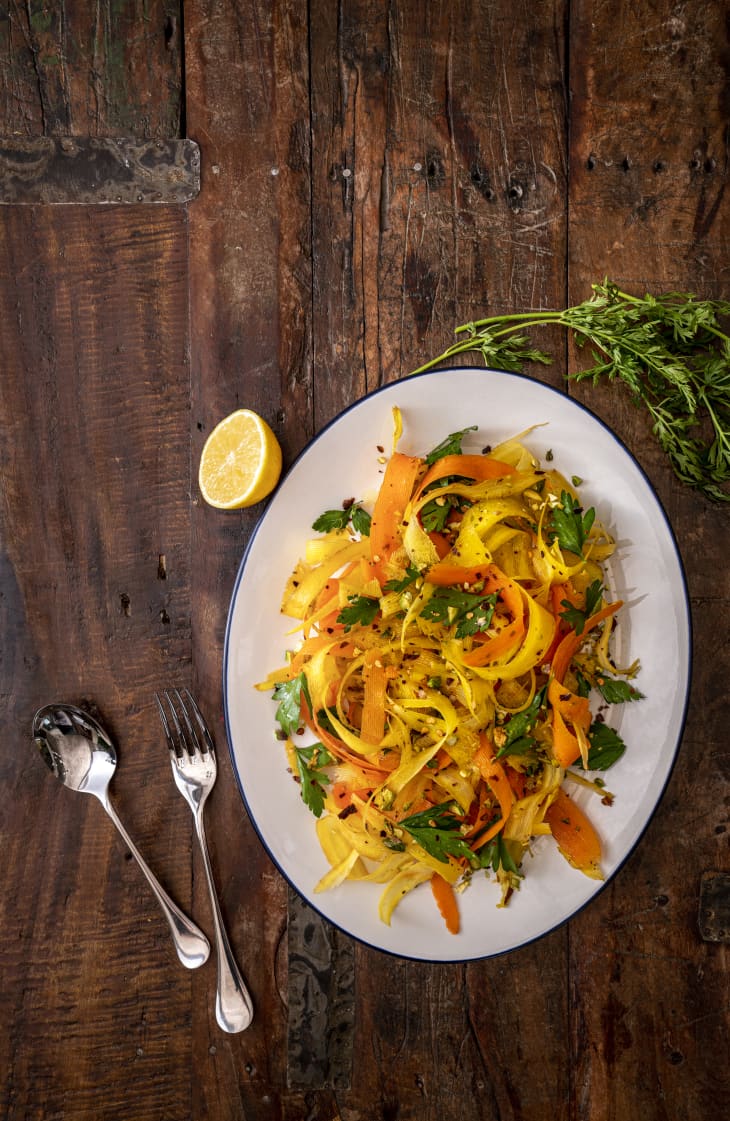 Shaved carrot and parsnip salad with parsley and lemon on a rustic wooden table, accompanied by cutlery.