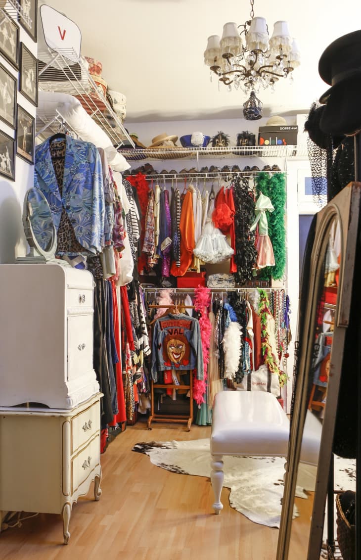 Eclectic closet with colorful clothes, vintage chandelier, white bench, and cowhide rug on wooden floor.