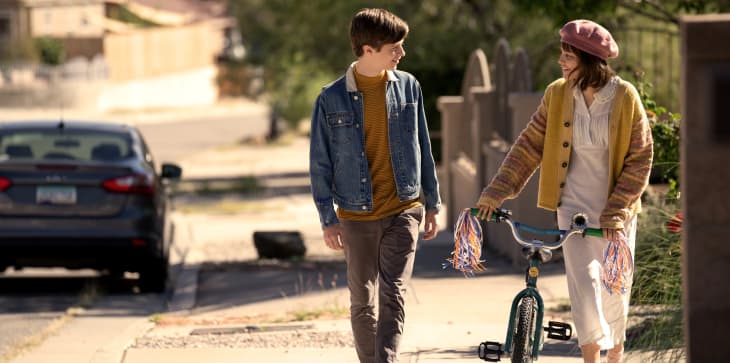 Two kids walking on a sidewalk; one holds a bike with colorful streamers.
