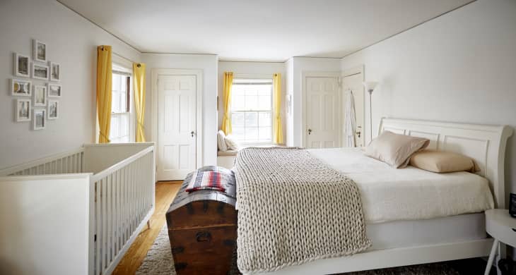 Bedroom with a white sleigh bed, wooden chest, crib, yellow curtains, and framed photos on the wall.