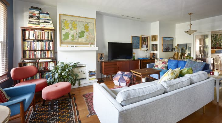Cozy living room with a gray sofa, blue armchair, red chairs, bookshelf, TV, and colorful cushions.