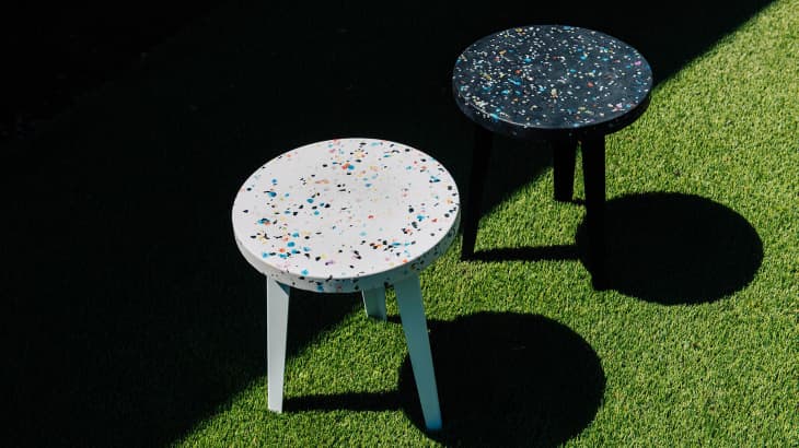 Two terrazzo tables, one white and one black, on green grass, casting shadows.