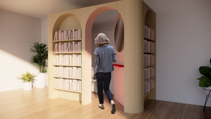 Woman entering a small reading nook with bookshelves and plants.