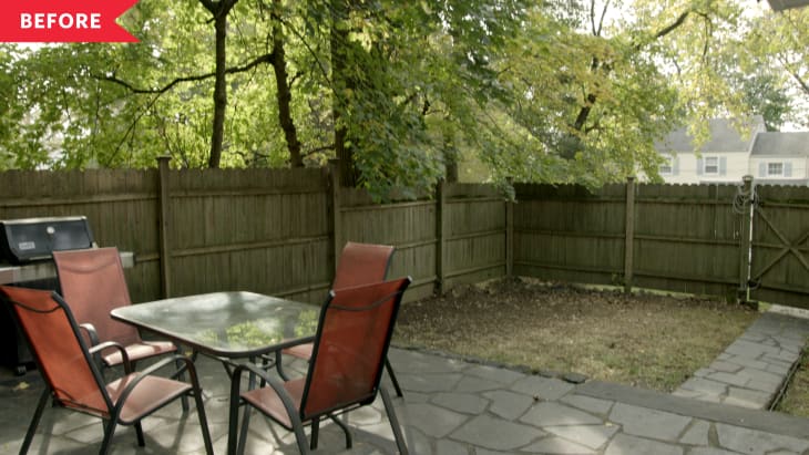 Patio with glass table, four red chairs, grill, and wooden fence surrounded by trees.