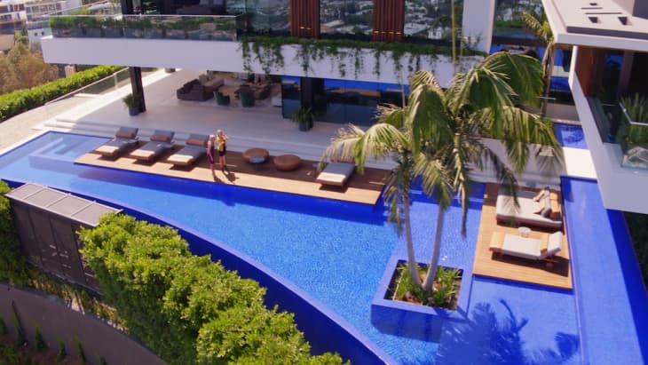 Modern luxury home with large blue pool, palm trees, sun loungers, and outdoor seating area.